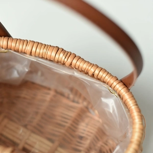 Close-up of handwoven wicker basket with leather handle and protective plastic liner