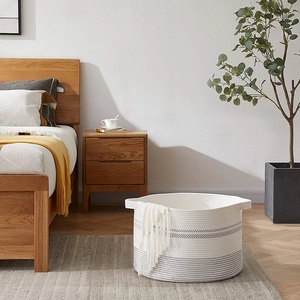 Handwoven cotton rope storage basket with gray base in a cozy bedroom setting