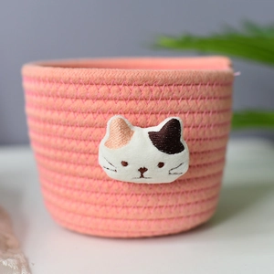 Pink round woven cotton rope storage basket featuring cute cat face embroidery detail