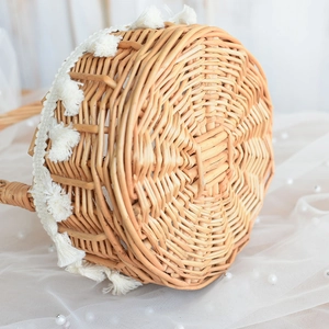 Detail of round woven rattan flower basket with white bohemian fringe on sheer fabric