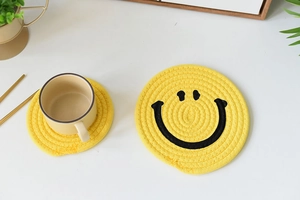 Detail view of a yellow woven cotton coaster with black smiley face and coffee cup