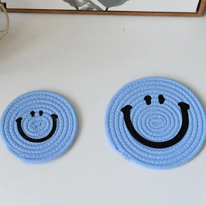Detail of round light blue woven coasters with black smiley face pattern in two sizes
