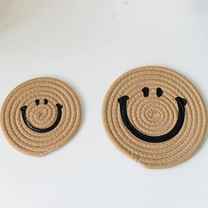 Detail of two handmade woven cotton coasters with black smiley face prints on a white surface