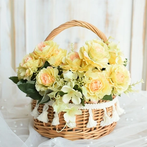 Detail of round rattan basket with pink faux peonies and white cotton tassels on wood