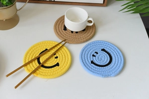 Detail of round woven cotton coasters with smiley face design in yellow and blue