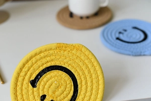 Detail of woven cotton cup coaster with yellow spiral texture and minimalist smile face