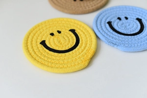 Close-up of woven cotton smiley face coasters in yellow and blue for heat insulation