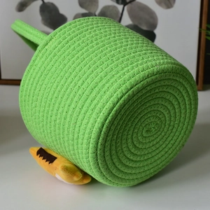 Detail of green woven storage basket showing spiral bottom texture and soft yellow pompom