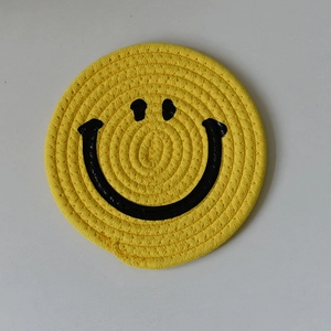 Handwoven yellow cotton rope coaster with a minimalist black smiley face design