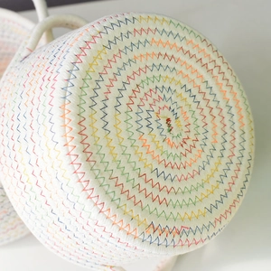 Close-up of circular woven cotton storage basket with rainbow wavy stitching and handle