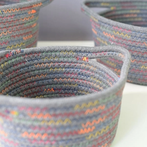Detail of dark grey woven cotton storage basket showing colorful wavy stitching and handle