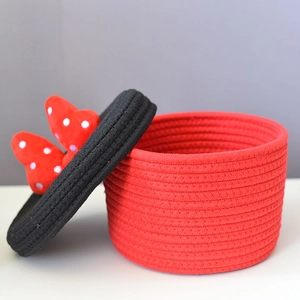 Close-up of handmade woven cotton rope storage basket with red bowknot on a black lid
