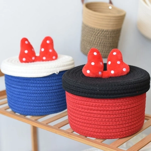 Close-up of cotton rope storage baskets with red polka dot bow lids on wooden shelf
