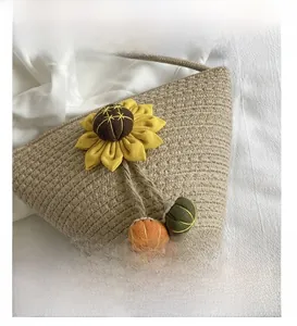 Close-up of beige woven straw bag featuring sunflower decor and colorful pompom tassels