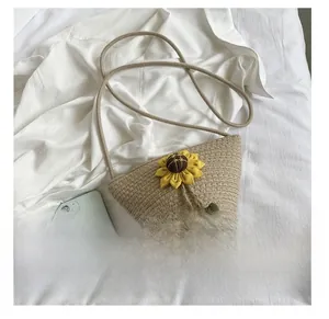 Detail view of woven straw beach bag featuring yellow sunflower and colorful pompom accents