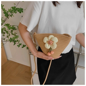 Detail of hand-woven straw bucket bag featuring 3D white floral decor and pink cherry charm