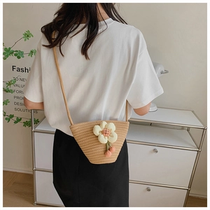 Detail of a beige woven mini bucket bag featuring a white 3D fabric flower on a model