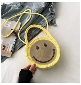 Détail d'un sac rond jaune tressé avec un motif de smiley scintillant en strass