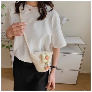 Detailed close-up of woven beige bucket bag with flower decor and pink pom-poms