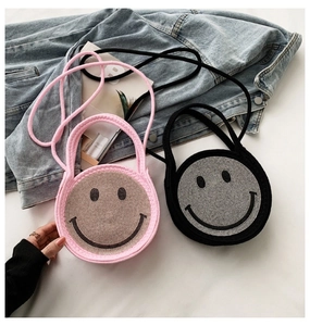 Détail du sac à bandoulière rond tissé avec décoration visage souriant en strass brillant
