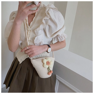 Mirror selfie showing a mini woven bucket bag with 3D flower charm and crossbody strap
