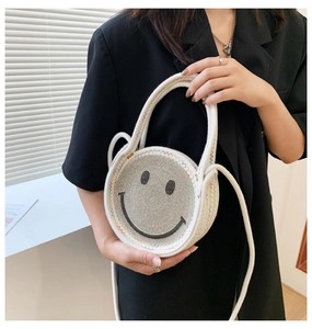 Détail d'un sac rond blanc tissé avec visage smiley en strass et bandoulière en coton
