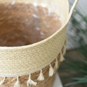 Detail of woven straw plant pot with decorative white tassels and waterproof liner