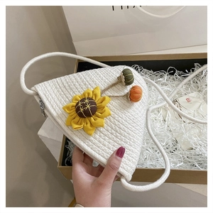 Detailed view of woven straw triangle bag featuring sunflower and colorful pompom charms