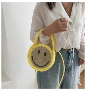 Sac rond en paille jaune porté en bandoulière avec un motif smiley brillant en strass
