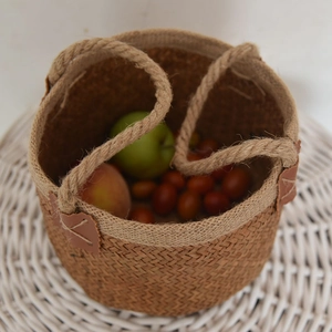 Natural woven jute storage basket with rope handles and fresh fruits on white background