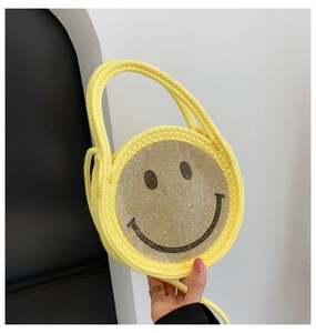 Détail du sac à main rond en paille tressée jaune avec un motif smiley en paillettes argent