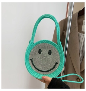 Détail d'un sac rond en paille vert avec un motif de smiley en strass étincelants