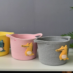 Detail view of woven cotton rope baskets with cute plush crocodile patches and handles