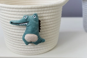 Detailed view of the woven cotton rope basket with a green plush crocodile decoration