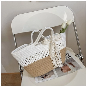 Detail of handmade woven tote bag featuring bicolor straw design and white lace bow accessory