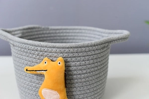 Close-up of grey woven cotton storage basket with handle and yellow dinosaur patch