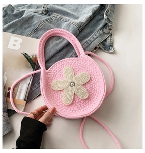 Détail d'un sac rond en tricot rose avec fleur de perle blanche et bandoulière tissée