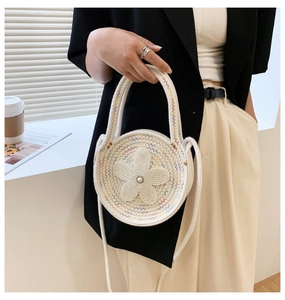 Détail d'un sac rond en tricot crème avec fleur en perles et poignée ronde