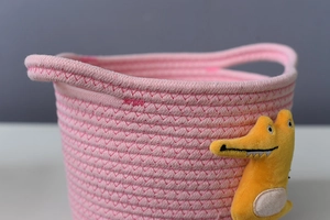 Detailed close-up of a pink woven cotton rope basket with yellow crocodile plush decor