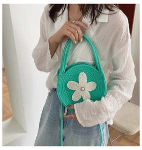 Détail d'un sac à main rond en tricot vert avec fleur blanche et perle