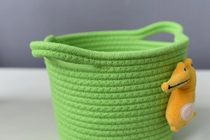 Detailed close-up of green cotton rope basket with yellow plush crocodile and handles