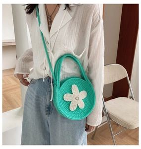 Détail d'un sac bandoulière rond tissé vert vif avec fleur blanche et perle