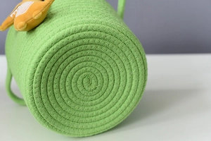 Detailed macro view of green woven cotton rope storage basket with cute yellow plush charm