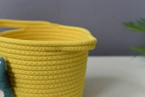 Detail shot of yellow cotton rope woven storage basket with green plush dinosaur decor