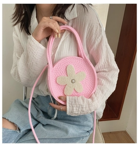 Petit sac rond rose tricoté avec fleur perlée porté par un mannequin en extérieur