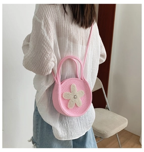 Détail du sac rond en tricot rose avec applique fleur blanche et perle sur la bandoulière