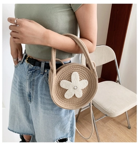 Détail d'un sac à main tissé beige rond avec fleur perlée blanche tenu par un modèle