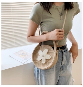 Détail d'un sac à bandoulière rond en paille avec fleur blanche et décor de perles