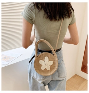 Vue détaillée d'un sac rond en paille kaki avec une fleur en crochet blanc et perle