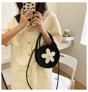 Détail du sac à bandoulière rond tressé noir avec une fleur blanche et une perle